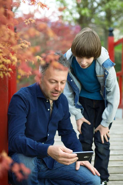 Father with teen son using smart phone outdoor together. Young b — Stock Photo, Image