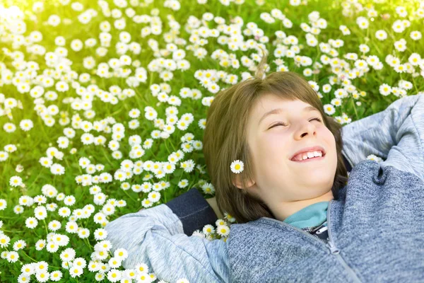 Красивый счастливый улыбающийся мальчик лежит на зеленом лугу — стоковое фото