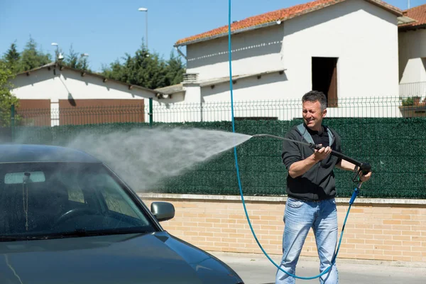 Car washing. Man cleaning car using high pressure water and brus