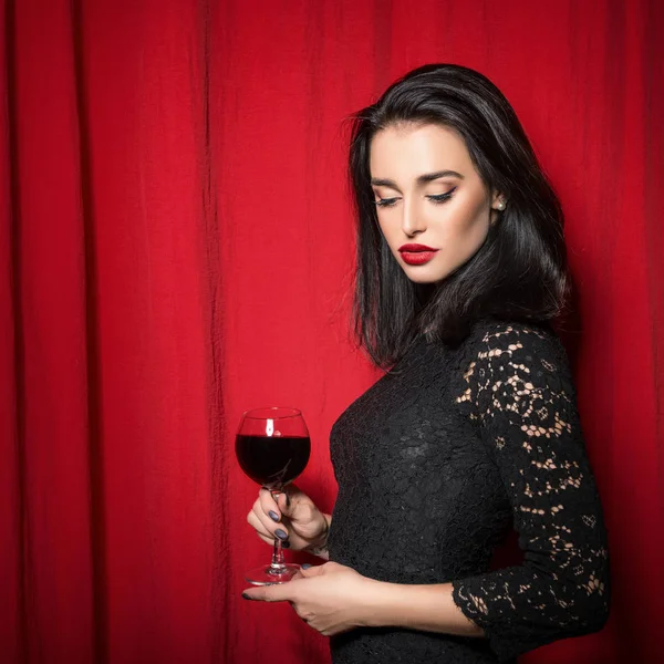 Joven hermosa mujer sosteniendo copa de vino sobre cortinas rojas —  Fotos de Stock