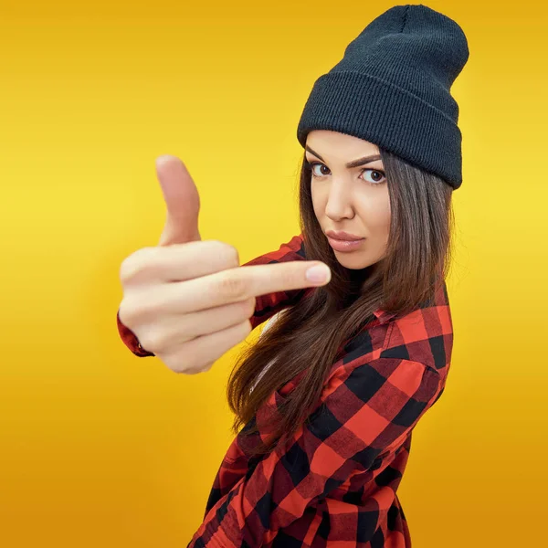 Hipster chica en jeans, camisa a cuadros y sombrero mostrando el medio f —  Fotos de Stock