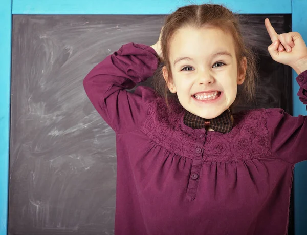 Cute liitle emotional girl standing near blackboard and happy sm — Stock Photo, Image