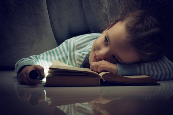 Menina lendo contos de fadas livro sob as capas na véspera — Fotografia de Stock