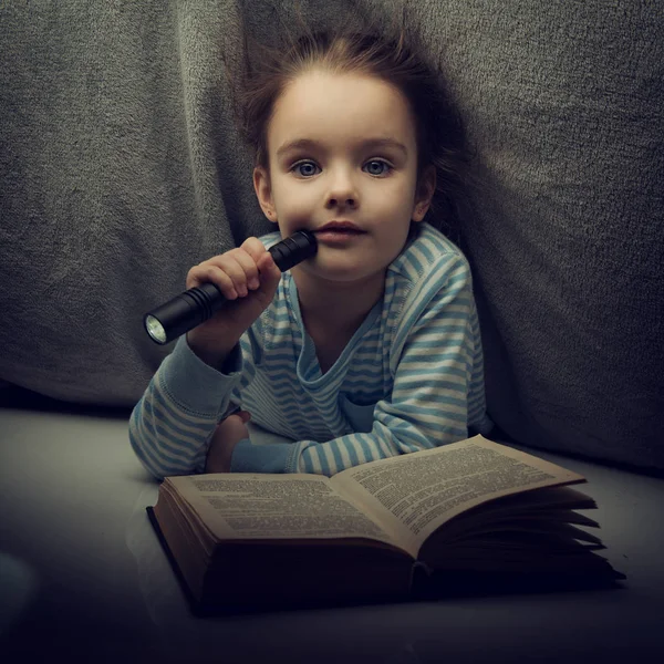 Niña leyendo cuentos de hadas libro bajo las cubiertas en la víspera — Foto de Stock