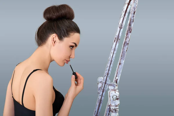 Retrato de una hermosa mujer sosteniendo lápiz labial y mirando al espejo — Foto de Stock