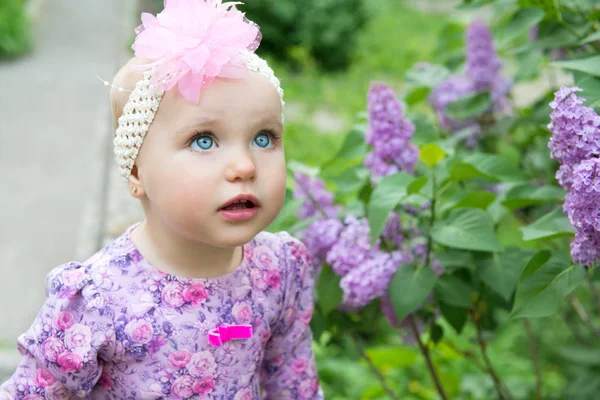 Bella bambina odora di fiori lilla nel parco primaverile. Bambino. — Foto Stock