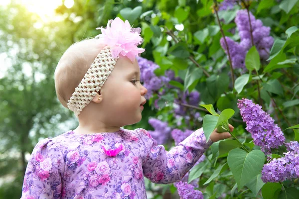 Bella bambina odora di fiori lilla nel parco primaverile. Bambino. — Foto Stock