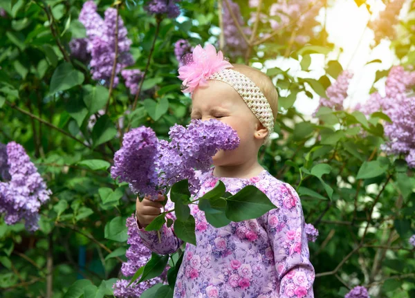 Bella bambina odora di fiori lilla nel parco primaverile. Bambino. — Foto Stock