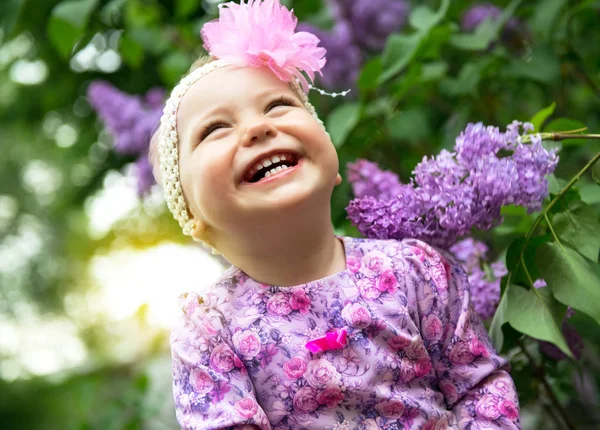 Красива маленька дівчинка грає у весняному парку, бузковий сад квітів — стокове фото