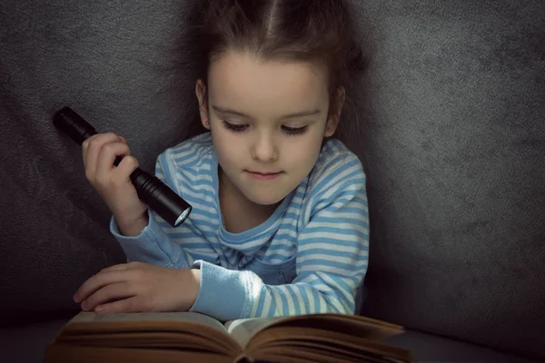 Маленька дівчинка читає казкову книгу під обкладинками напередодні — стокове фото