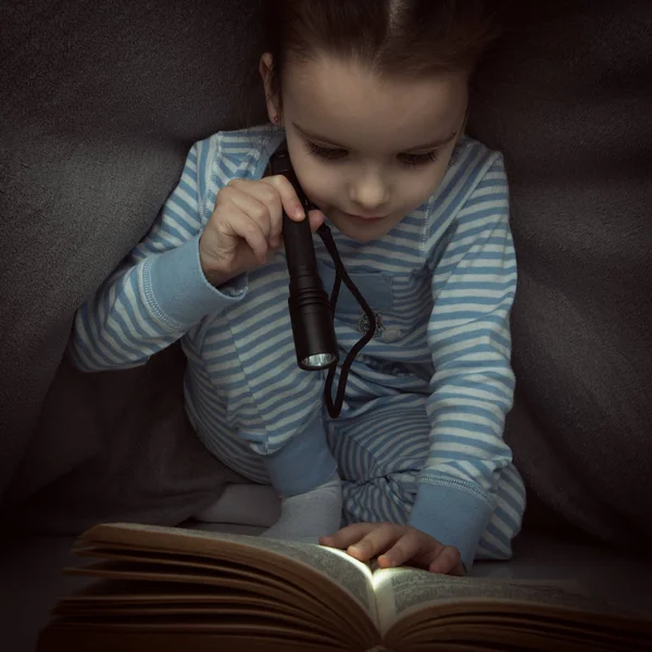 Niña leyendo cuentos de hadas libro bajo las cubiertas en la víspera —  Fotos de Stock