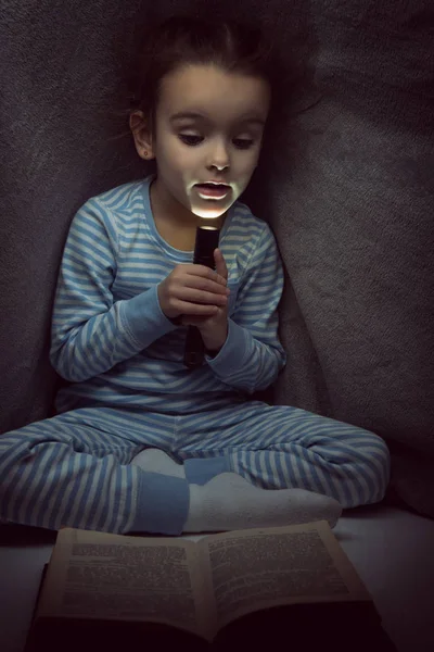 Kleines Mädchen liest am Vorabend unter dem Cover ein Märchenbuch — Stockfoto