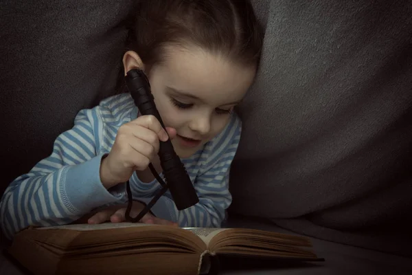 Niña leyendo cuentos de hadas libro bajo las cubiertas en la víspera —  Fotos de Stock