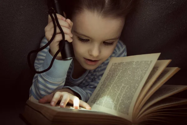 Niña leyendo cuentos de hadas libro bajo las cubiertas en la víspera — Foto de Stock