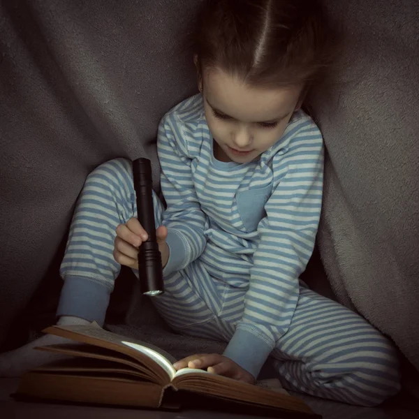 Niña leyendo cuentos de hadas libro bajo las cubiertas en la víspera — Foto de Stock