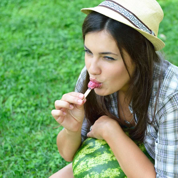 Ung kvinne som spiser iskrem og holder vannmelon utendørs i s. – stockfoto