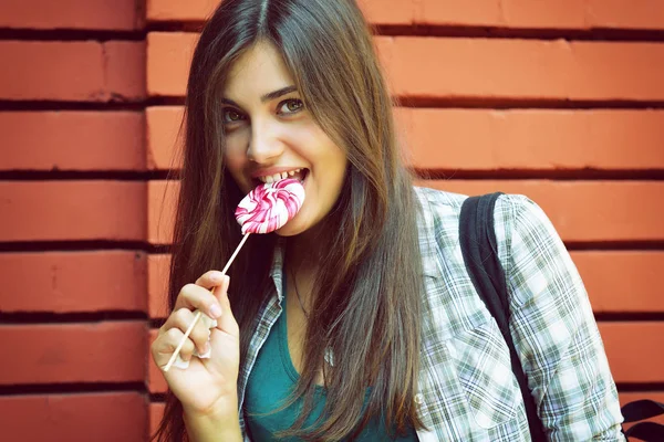 Menina bonita tem diversão e lambendo doces doces ao ar livre contra r — Fotografia de Stock