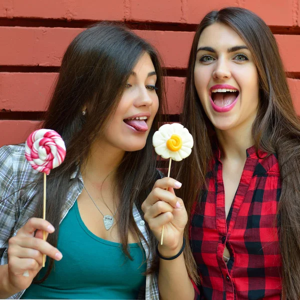 Dos hermosas chicas se divierten abrazando y lamiendo dulces dulces o —  Fotos de Stock
