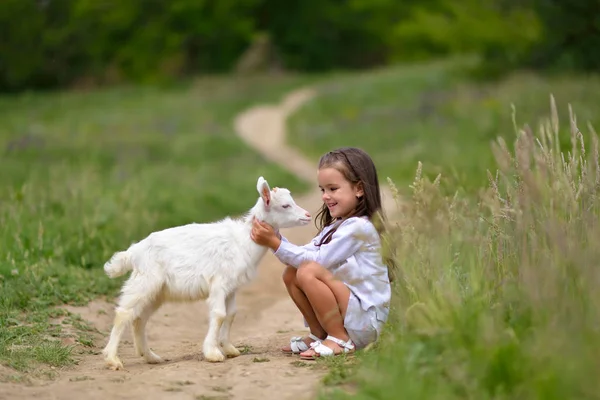 Petite fille joue et huhs chèvre à la campagne, au printemps ou en été — Photo
