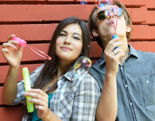 Young attractive happy boy and girl blow soap bubbles outdoor ag — Stock Photo, Image