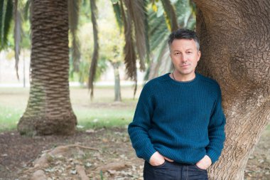 Akdeniz parkında palmiye ağaçları olan yakışıklı, orta yaşlı bir adam. Çekici orta yaşlı erkek model aykırı poz veriyor. 