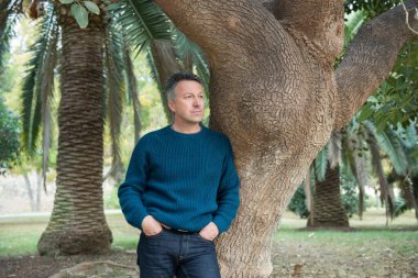 Akdeniz parkında palmiye ağaçları olan yakışıklı, orta yaşlı bir adam. Çekici orta yaşlı erkek model aykırı poz veriyor. 