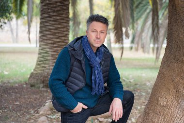 Akdeniz parkında palmiye ağaçları olan yakışıklı, orta yaşlı bir adam. Çekici orta yaşlı erkek model aykırı poz veriyor. 