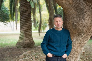 Akdeniz parkında palmiye ağaçları olan yakışıklı, orta yaşlı bir adam. Çekici orta yaşlı erkek model aykırı poz veriyor. 