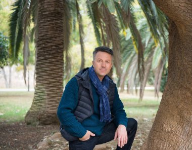 Akdeniz parkında palmiye ağaçları olan yakışıklı, orta yaşlı bir adam. Çekici orta yaşlı erkek model aykırı poz veriyor. 