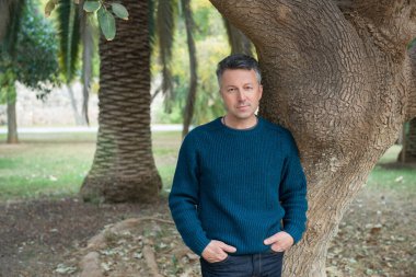 Akdeniz parkında palmiye ağaçları olan yakışıklı, orta yaşlı bir adam. Çekici orta yaşlı erkek model aykırı poz veriyor. 