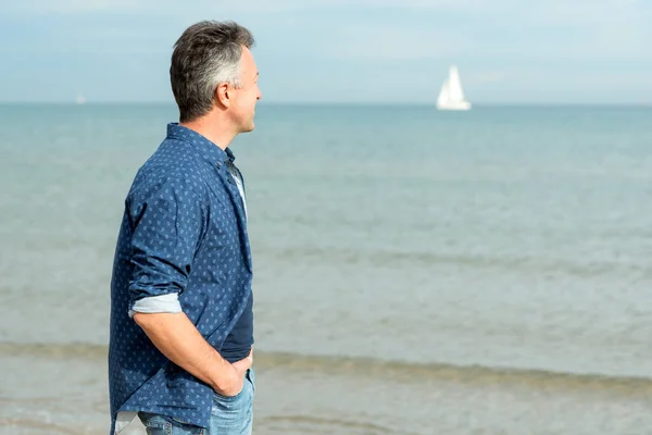 ハンサムな中年の男性は ビーチで歩いている 青いジーンズ Tシャツで海辺にポーズをとる魅力的なミッド大人の男性モデル 美しい町の男の屋外の肖像画 — ストック写真