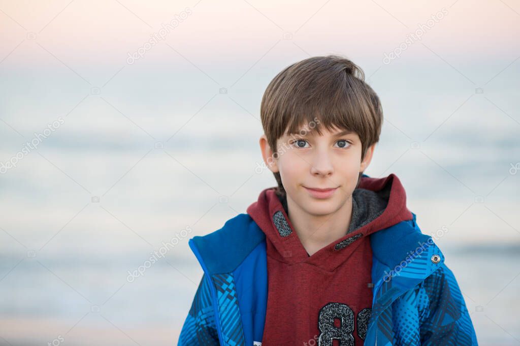 Young boy posing at the winter beach. Cute smiling happy 11 years old boy at seaside, looking at camera. Kid's outdoor portrait.