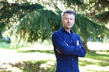 Parkta, çam ağacının yanında yakışıklı, orta yaşlı bir adam. Çekici orta yaşlı erkek model aykırı poz veriyor. 