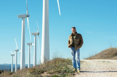 Açık havada mavi gökyüzüne karşı rüzgar türbiniyle insan portresi. Yel değirmeni jeneratörleri. Rüzgar jeneratörleri.