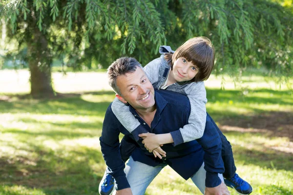 夏の公園で楽しんでいる彼の息子と父親の肖像画 ピギーバック 家族の楽しみ パパの夏の自然屋外で遊んで幸せな男の子 子育て — ストック写真