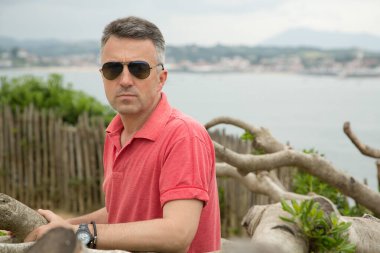 Kumsalda poz veren orta yaşlı yakışıklı bir adam. Deniz kenarında poz veren çekici orta yaşlı erkek model. Güzel bir adamın açık hava portresi, görüntü tonlu..