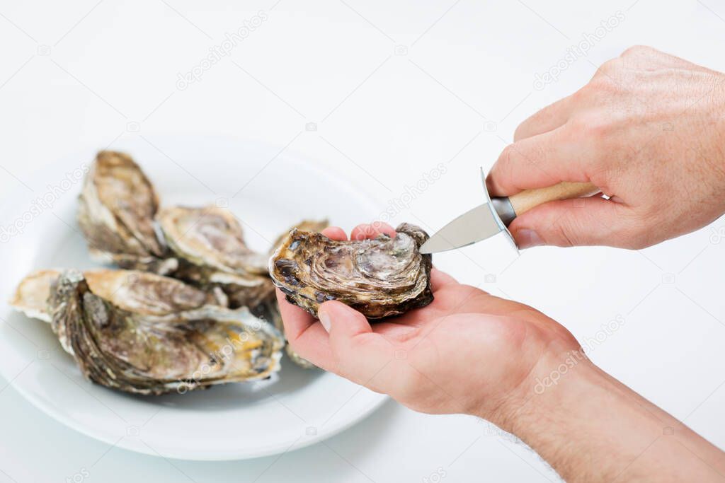 Fresh oyster. Man open fresh oyster. Raw fresh oyster is on white round plate, image isolated, with soft focus. Restaurant delicacy. Saltwater oyster.