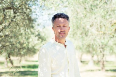 Zeytin ağaçları. Zeytin bahçesinde poz veren yakışıklı bir adam. Akdeniz zeytin tarlasında hasat için hazır erkek portreleri. İtalyan zeytinliğinde kendine güvenen olgun bir adam taze zeytinlerle dolu. Taze zeytin. Zeytin çiftliği