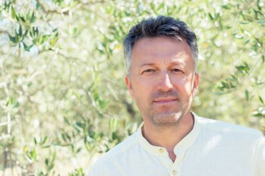 Zeytin ağaçları. Zeytin bahçesinde poz veren yakışıklı bir adam. Akdeniz zeytin tarlasında hasat için hazır erkek portreleri. İtalyan zeytinliğinde kendine güvenen olgun bir adam taze zeytinlerle dolu. Taze zeytin. Zeytin çiftliği