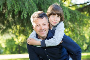 Baba ve oğlunun yaz parkında eğlenirken portresi. Sırtına al. Aile eğlencesi. Mutlu çocuk babasıyla oynuyor yaz doğası açık havada. Ebeveynlik. İki kuşak.