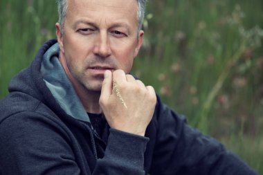 Yaz çayırlarında çim biçme bıçağıyla poz veren ve kameraya bakan yakışıklı orta yaşlı bir adamın portresi..