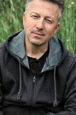 Yaz çayırında kameraya bakarak poz veren orta yaşlı yakışıklı bir adamın portresi..