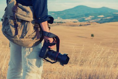 Toskana 'da dijital kameralı profesyonel bir fotoğrafçı yürüyor. Fotoğraf makinesi erkeklerin yaz mevsiminde Toskana 'da tarlaları, mavi gökyüzü ve dağları, İtalya, Avrupa. 