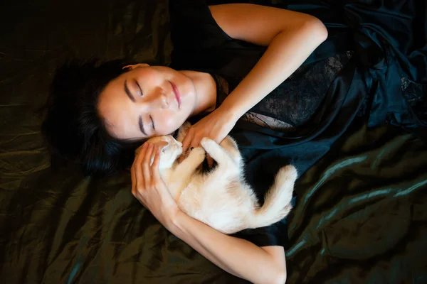 パジャマを着た美しい中国の若い女性が子猫とベッドで寝ています おはようございます 寝室で子猫ちゃんと寝ちゃった 甘い夢 — ストック写真