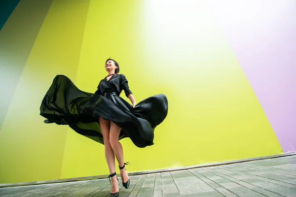 ファッションの女性 若い美しい中国の女の子は カラフルな壁の背景に高いヒールで長い黒のドレスを着て屋外で踊る スタイリッシュな流行の女性 — ストック写真