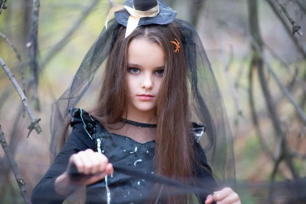 美丽的小女孩 一头乌黑的长发 穿着巫婆裙 头戴帽子 带着恐惧的表情走在秋天的森林里 万圣节的恐怖 黑暗中的女巫 — 图库照片