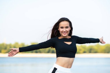 Çekici esmer kız gülümsüyor ve dışarıdaki hayattan zevk alıyor. Genç kadın, yaz portresi. Doğada nehir, sahil ve mavi temiz gökyüzü ile poz veren kadın model. Özgürlük, gençlik yaşam tarzı, aktif eğlence