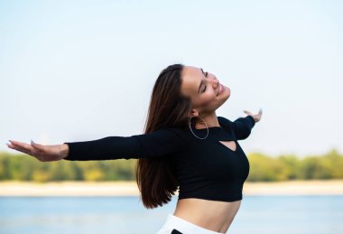 Çekici esmer kız gülümsüyor ve dışarıdaki hayattan zevk alıyor. Genç kadın, yaz portresi. Doğada nehir, sahil ve mavi temiz gökyüzü ile poz veren kadın model. Özgürlük, gençlik yaşam tarzı, aktif eğlence