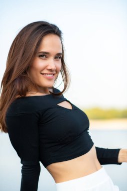 Açık havada gülümseyen güzel esmer kız. Genç kadın, yaz portresi. Doğada nehir, sahil ve mavi temiz gökyüzü ile poz veren kadın model..