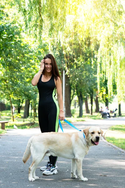 陽気かなり若い女性が夏の公園で彼女の犬と歩いて実行しています アクティブレジャー 美しいですブルネット女の子とともに午前ジョギングとともに子犬 — ストック写真